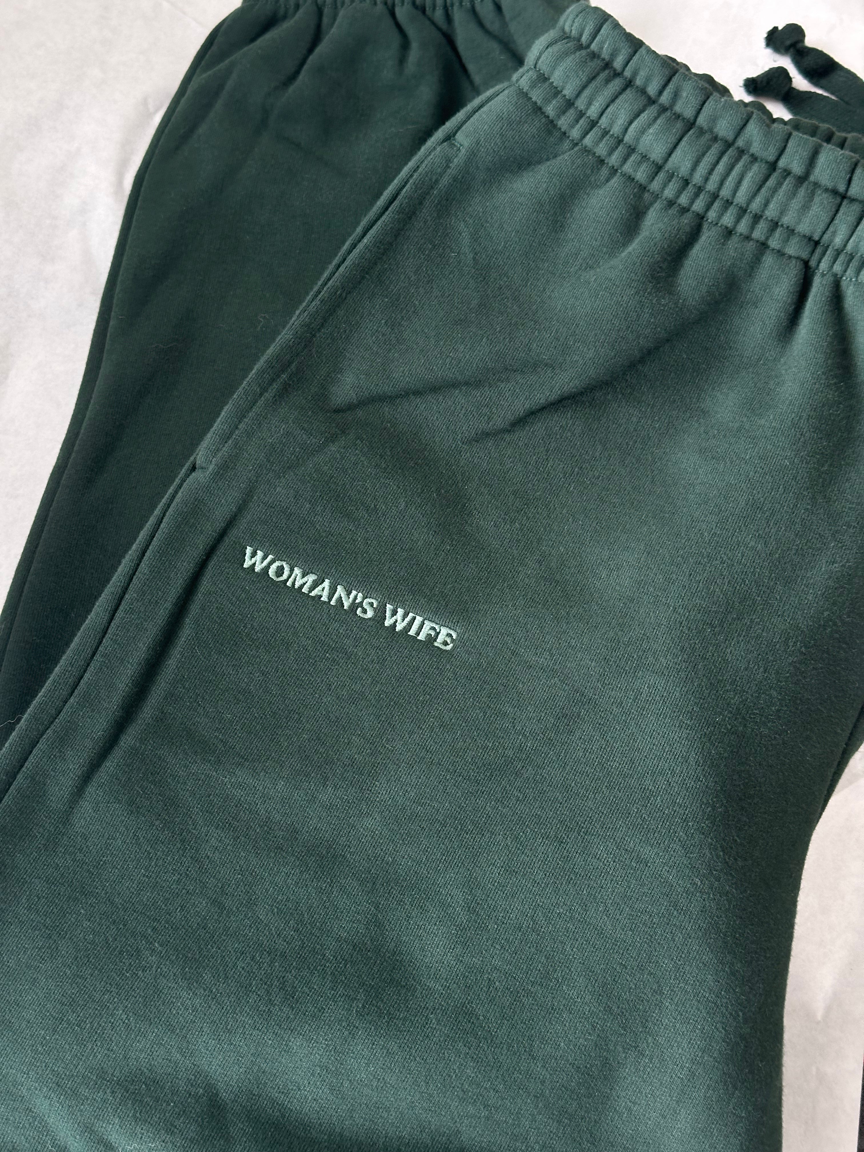 Green sweatpants with 'WOMAN'S WIFE' text on a light background