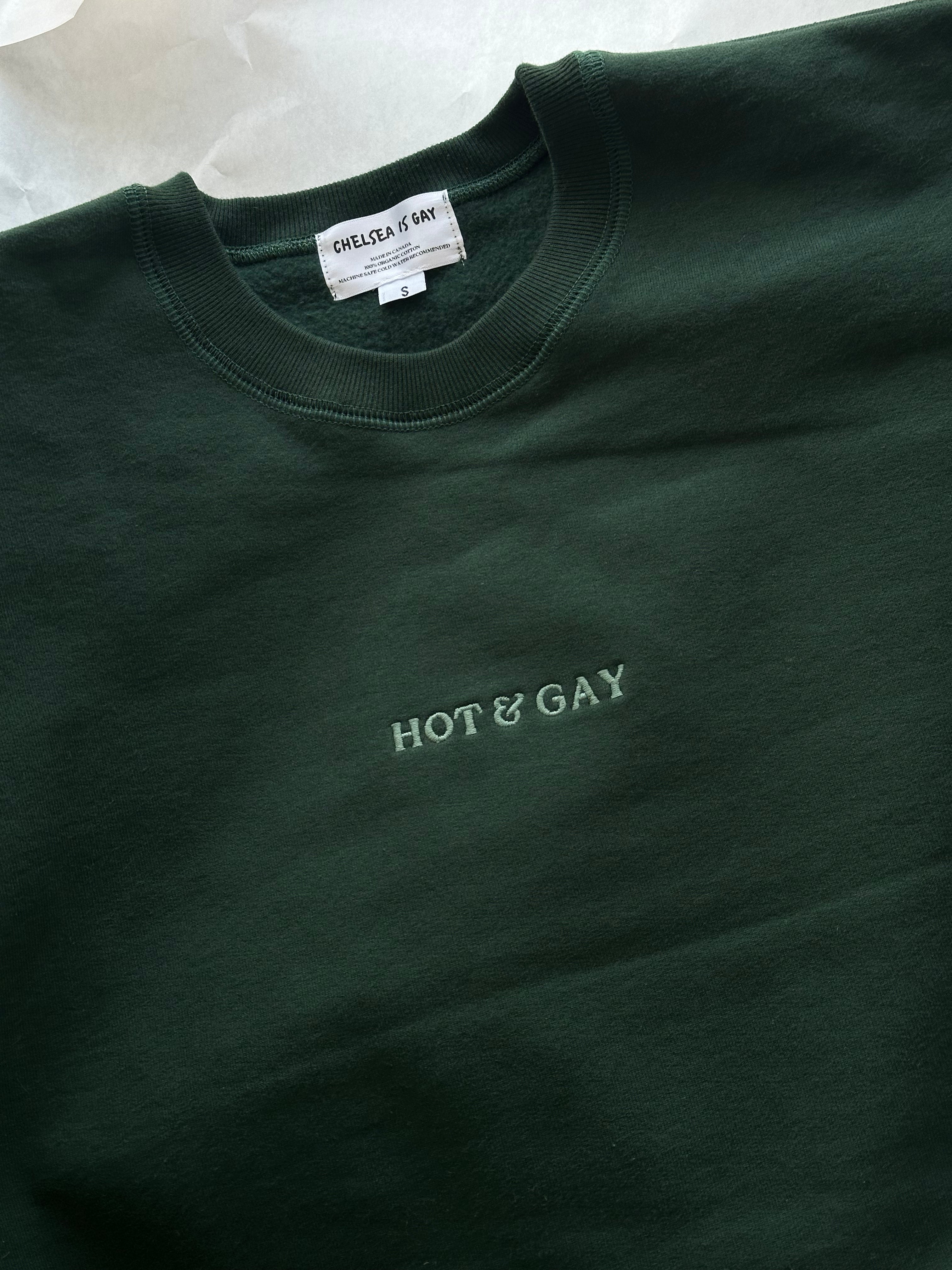 Dark green sweatshirt with 'HOT & GAY' embroidery text and a 'Chelsea is Gay' tag on a white background