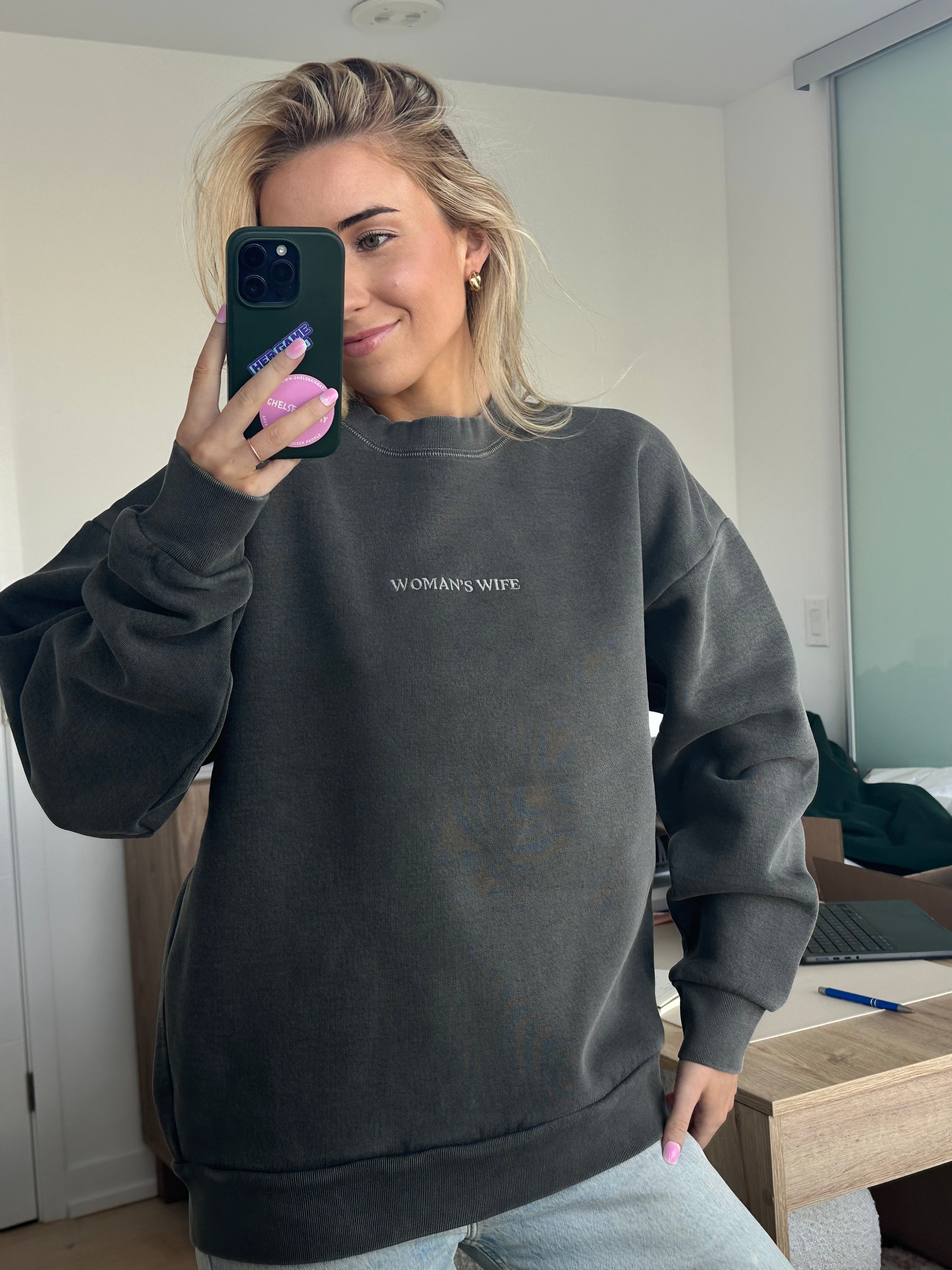 Person wearing a dark gray sweatshirt with 'WOMAN'S WIFE' text, taking a mirror selfie.