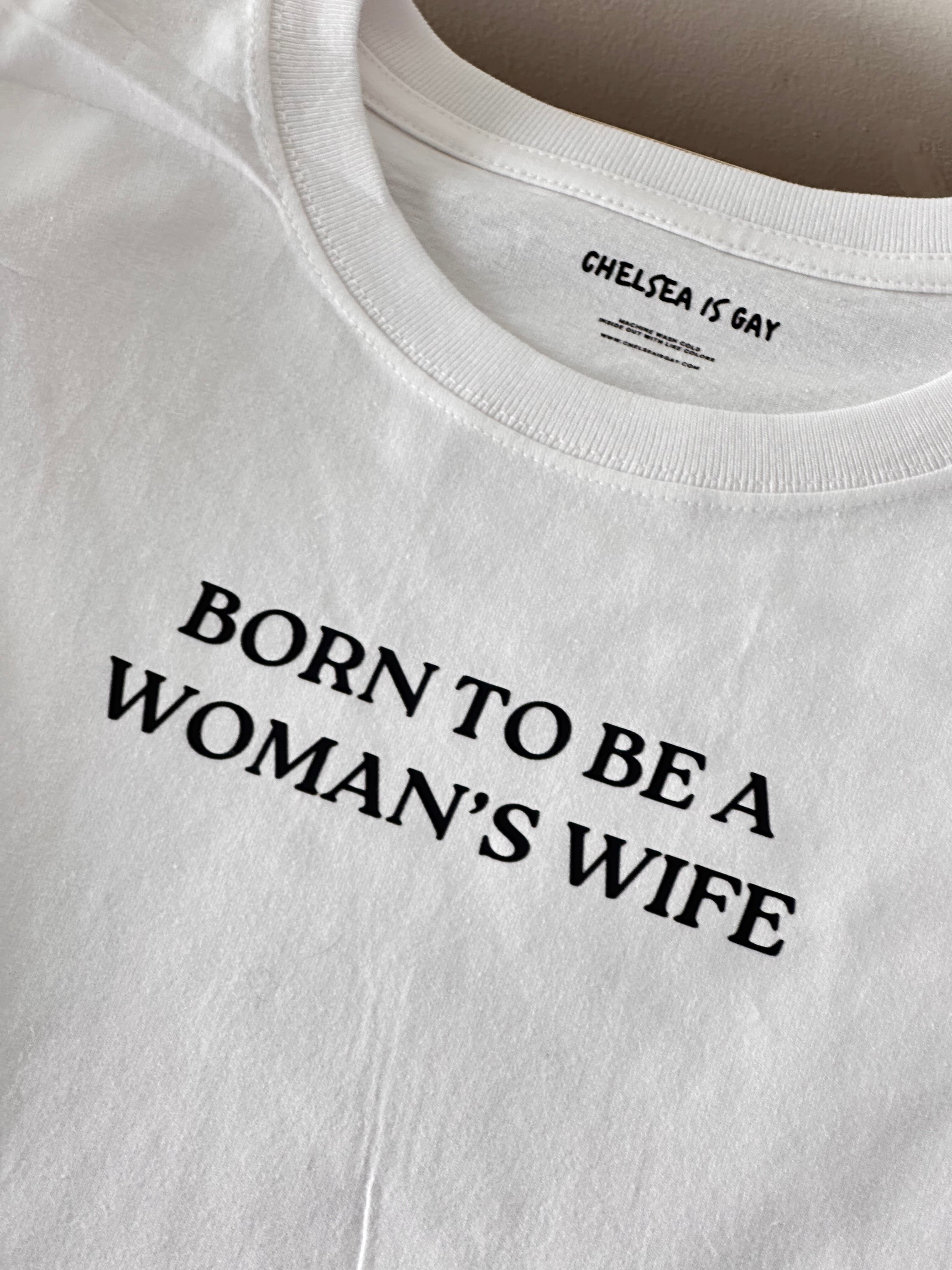 White t-shirt with black text 'BORN TO BE A WOMAN'S WIFE' on a white background